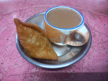 A small steel plate with one potato samosa and a cup of teaの写真素材