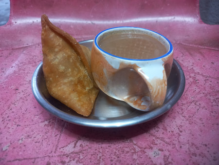 A small steel plate with one potato samosa and a cup of teaの写真素材