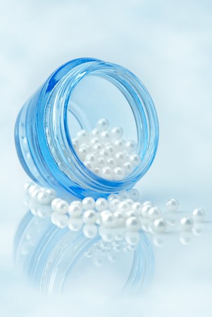 Beauty concept. Cosmetic container full of natural pearls over sky imitating background. Blue tinted, shallow depth of fieldの写真素材