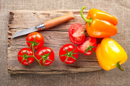 Fresh tomato, paprika, steel knife and vintage wooden cutting board on canvas tableclothの写真素材