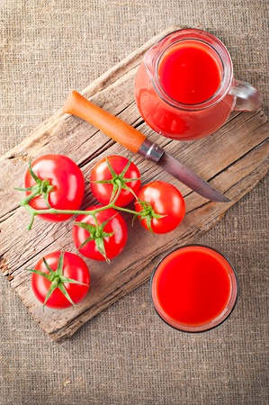 Tomato juice in glass jar, fresh tomatoes, steel knife on vintage wooden cutting board and linen backgroundの写真素材
