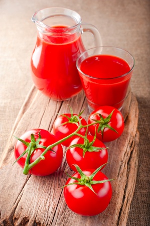 Tomato juice in jar and fresh tomatoes on vintage wooden cutting board and linen background. Shallow depth of fieldの写真素材