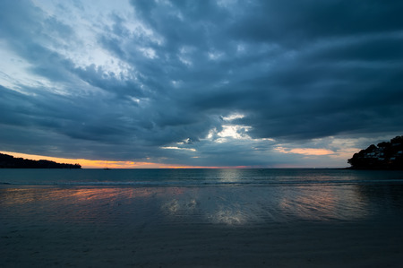 Sunset at tropical sandy beach. Blue colors of evening ocean landscape under dramatic stormy sky. Phuket, Thailandの写真素材