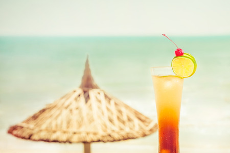 Long Island cocktail with fruits decoration at tropical ocean beach with umbrella  Vintage style, hipster colors image with copy space for party invitation textの写真素材