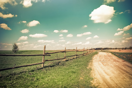 Sunny day in countryside. Empty rural road going through summer landscape under blue cloudy sky. Nature background in vintage styleの写真素材