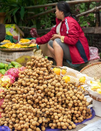 LUANG PRABANG, LAOS - DEC 8: Unidentified woman selling  longan and other tropical fruits at traditional asian food marketplace on Dec 8, 2013 in Luang Prabang, Laosのeditorial素材