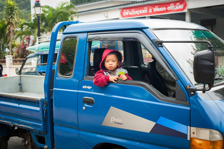 LUANG PRABANG, LAOS - DEC 8: Unidentified cute boy looks out the window of his father cargo car at asian city street on Dec 8, 2013 in Luang Prabang, Laosのeditorial素材