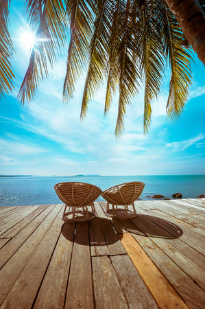 Amazing tropical beach landscape with palm tree and chairs for relaxation on wooden terrace. Travel background in vintage styleの写真素材