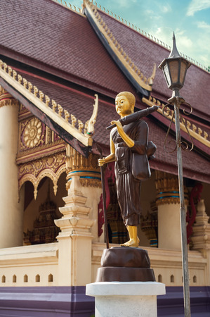 Statue of walking Buddha in traditional theravada style with umbrella and bowl. Asian city religious architecture at public place. Vientiane, Laosの写真素材