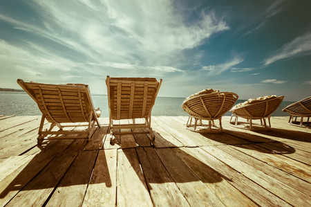 Amazing tropical beach landscape with chairs for relaxation on wooden terrace. Travel background in vintage styleの写真素材