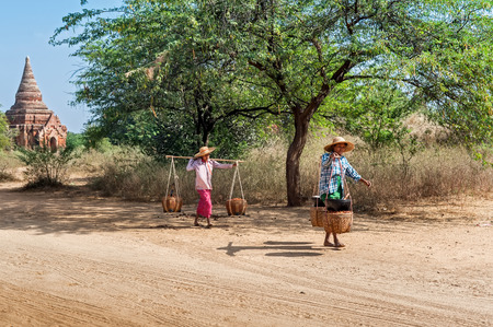 BAGAN, MYANMAR - JANUARY 16, 2014: Burmese rural women carrying baskets with berries harvest. Burma travel destinations with ancient Buddhist Temples and local people at Bagan Kingdomのeditorial素材