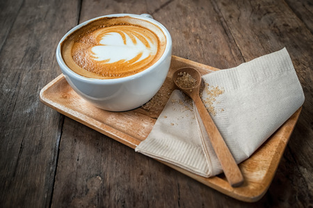 Cup of cappuccino coffee on wooden plate and brown sugar in spoon. Food background in vintage styleの写真素材