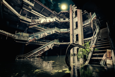 Dramatic view of damaged escalators in abandoned building. Full moon shining on cloudy night sky through collapsed roof. Apocalyptic and evil conceptの写真素材