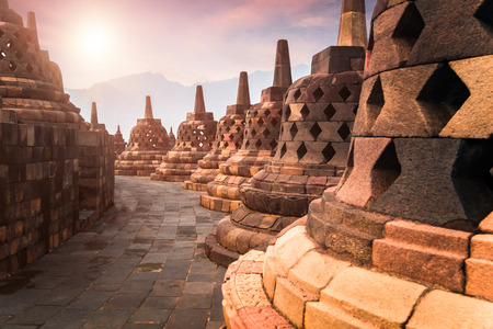 Amazing sunrise view of stone stupas at ancient Borobudur Mahayana Buddhist temple against shining...