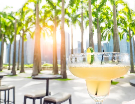 Drinking margarita cocktail in Singapore outdoors cafe. Amazing sunset cityscape  with palm trees and skyscrapers. Luxury vacation in modern asian cityの写真素材