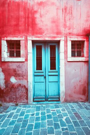 Old scratched blue door and small windows at colorful red house wall, Abstract view of city street with abandoned building. Shabby texture and grunge urban background. Greeceの写真素材
