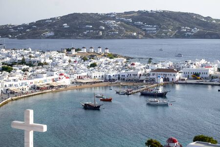 Panorama of sunset above Mykonos town harbor with Greek Orthodox church cross in front. Old windmills (Kato Mili)- famous landmark and tourist attraction on background. Ships on Aegean sea, Cycladesの写真素材