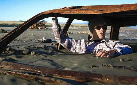 Man sits in rusted car wreck buried in sand on beachの写真素材