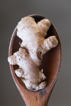 Ginger root on a wooden spoon with a grey backgound