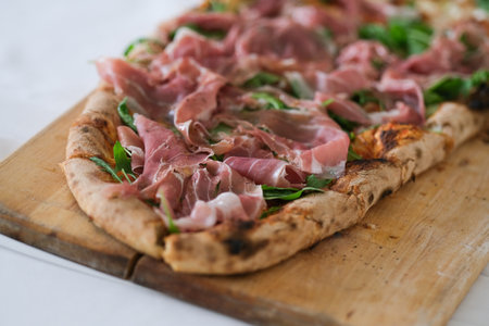 Pizza with ham on a wooden plateの写真素材