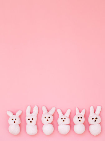 White handmade marshmallow candy bunnies on pink paper background with copy space for your Easter text message. Minimal happy Easter holiday concept. Top view flat lay, border frame, verticalの写真素材