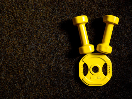 yellow heavy dumbbells and barbell metal weight disc in shape of Easter bunny on black background. Easter fitness and training composition with copy space. Top view from above, flat layの写真素材