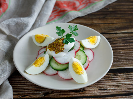 Plate with healthy spring vegetarian salad with radish, cucumber, egg and parsley with sour cream. and mustard, top view on wooden background with fork and napkin, russian summer foodの写真素材