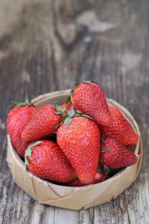 Fresh strawberries in a bamboo bowl on an old wooden background, vertical, copy spaceの写真素材