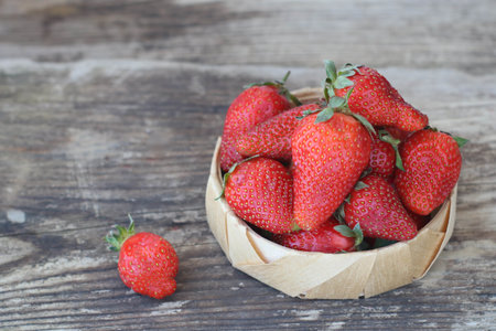 Fresh strawberries in a bamboo bowl and one berry on an old wooden background, horizontal, copy spaceの写真素材