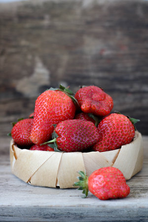 Fresh strawberries in a bamboo bowl on an old wooden background, vertical, copy space, side viewの写真素材