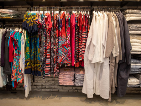 Beautiful colorful women clothing dress, wardrobe and t-shirts hang on hangers inside of a shopping mall. elegant clothes. women fashion industry. Classic design. Merchandise in a shopの写真素材