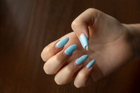 Damaged nail polish of blue color on the regrowth nails of the hand with white skin. Need in correction. Dark wooden background with space for text. close-up. selective focus. Horizontalの写真素材