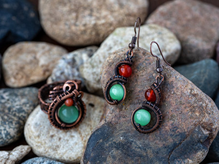 Unique handmade jewelry ring and earrings made of wrapped copper wire and colorful stones red jasper or cornelian and green chrysoberyl cats eye lying on natural stones. Horizontalの写真素材