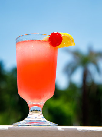 Glass of non alcoholic pink Strawberry lemonade cocktail on table or balcony at tropical resort with palm tree. vertical, close up. Healthy fresh cold drink. Vegetarian cocktail party. copy spaceの写真素材