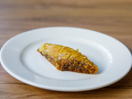 rhomb piece of honey baklava with walnut on white plate on wooden table background Traditional turkish dessert Oriental sweet pastry. close up.の写真素材