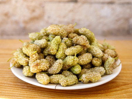 Fresh white mulberry on plate on wooden background. (Morus alba) Side view close-up. Summer organic fruits. Mulberry backgroundの写真素材