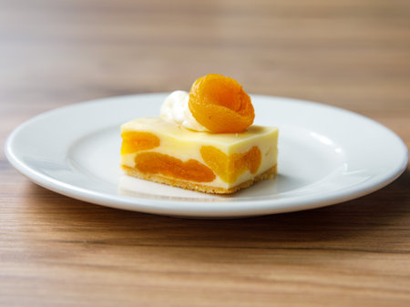 Delicious dried apricot mousse cake slice with white chocolate cream on top on wooden table background. Restaurant menu and confectionery concept. close-up. copyspace.の写真素材