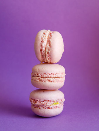 tower of pink pastel macaroons close-up on bright purple background, Stack of three pink strawberry raspberry cookies. Verticalの写真素材