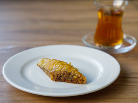 rhomb piece of honey baklava with walnut on white plate on wooden table background with turkish glass of tea in shape of tulip, named bardak. Traditional turkish dessert Oriental sweet pastry Close upの写真素材