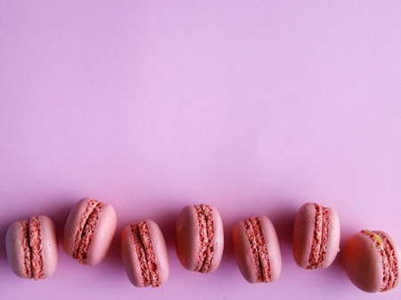 border of pink pastel macaroons close-up on light purple background. Blueberry, black currant, lavender strawberry raspberry cookies. Vertical or horizontal, copy space, top view, flat layの写真素材