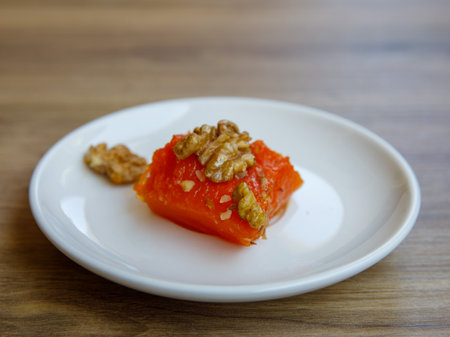 Traditional Turkish dish of baked walnut pumpkin Kabak tatlisi on white plate on a wooden table background. Delicious healthy dessert close-upの写真素材