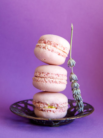 tower of pink pastel macaroons close-up on metal vintage plate on bright purple background with lavender flower, Stack of three pink strawberry raspberry cookies. Verticalの写真素材