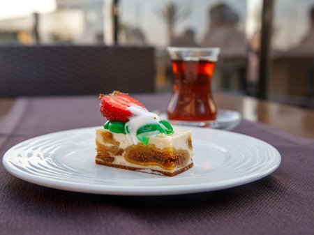 Delicious fig mousse cake slice with white chocolate cream and strawberry on top and black tea on table background in outside cafe. Restaurant menu and confectionery concept. close-up. copyspace.の写真素材