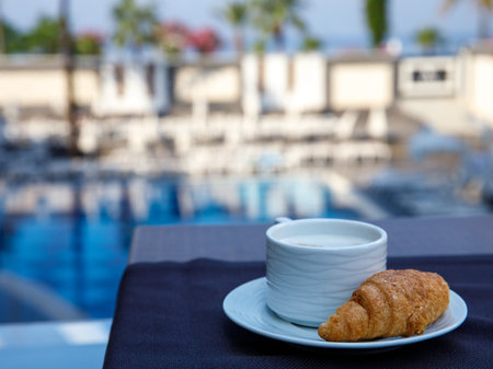 Delicious breakfast croissant and coffee on table ob balcony at the swimming pool in luxury hotel resortの写真素材