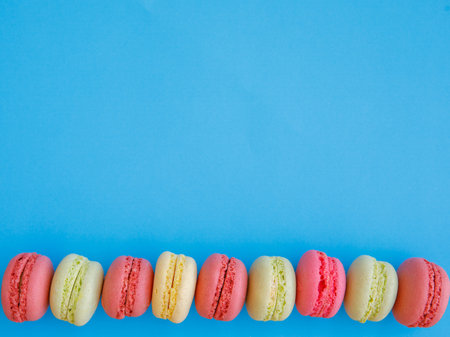 Delicious colorful Macarons almond cookies diffrent colors and flavor on bright blue background. Top view flat lay food photography. Mockup, free copy space for text, border, vertical or horizontalの写真素材