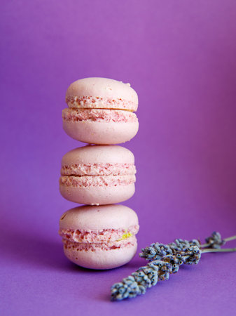 tower of pink pastel macaroons close-up on bright purple background with lavender flower, Stack of three pink strawberry raspberry cookies. Verticalの写真素材