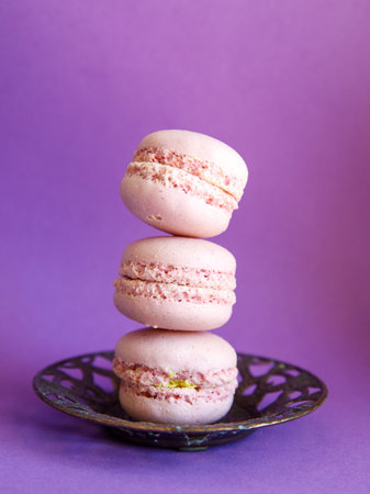 tower of pink pastel macaroons close-up on metal vintage plate on bright purple background, Stack of three pink strawberry raspberry cookies. Verticalの写真素材