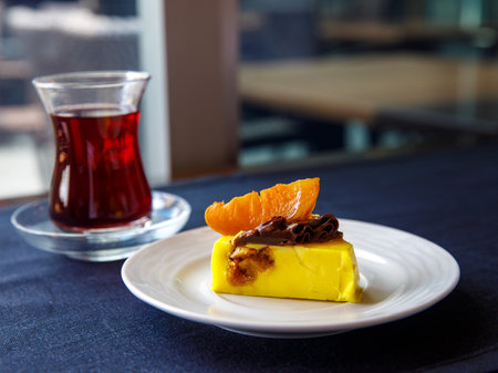 Delicious banana mango orange mousse cake slice with chocolate cream and caramelized orange on top on black table background. Restaurant menu and confectionery concept. close-up. copyspace.の写真素材
