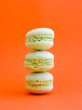 tower of mint green pastel macarons close-up on bright orange background, Stack of three pistachio or green tea cookies. Verticalの写真素材