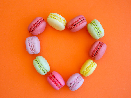 Delicious colorful Macarons almond cookies diffrent colors and flavor on bright orange background in shape of heart. Top view flat lay food photography. Mockup, free copy space for text, frameの写真素材